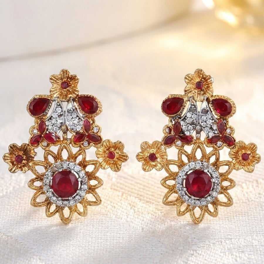 Close-up of deep red floral gemstone earrings displayed on soft white fabric with warm lighting