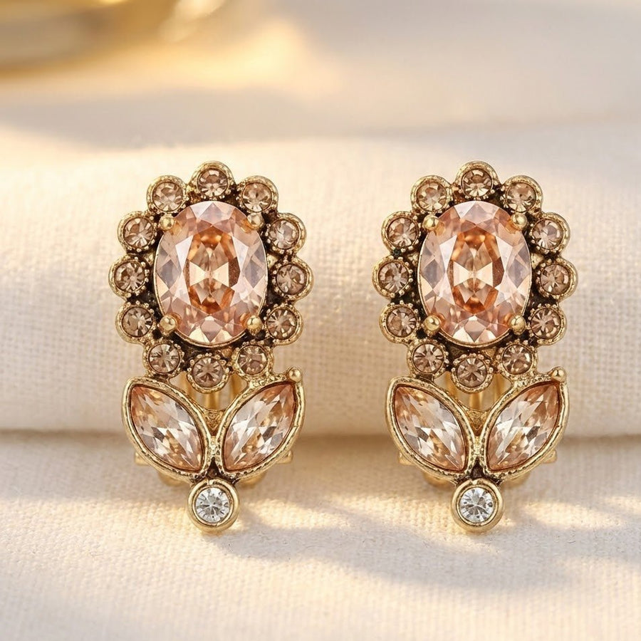 Close-up of gold-tone floral earrings resting on beige fabric background showing intricate crystal details