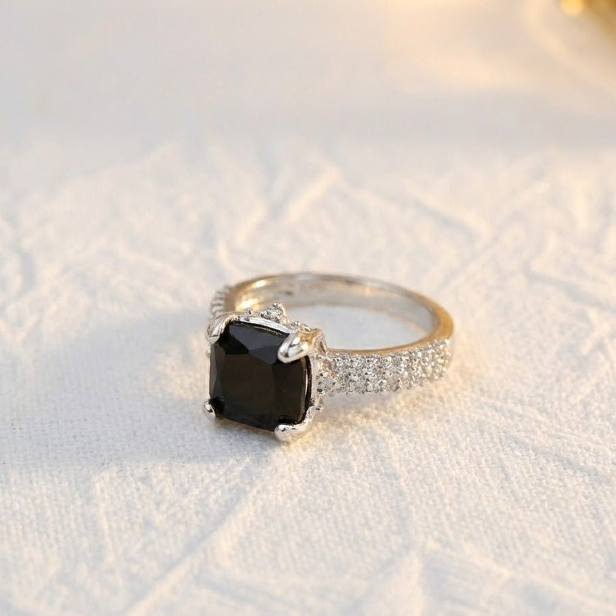 Silver cocktail ring with black cushion-cut gemstone placed on white textured fabric