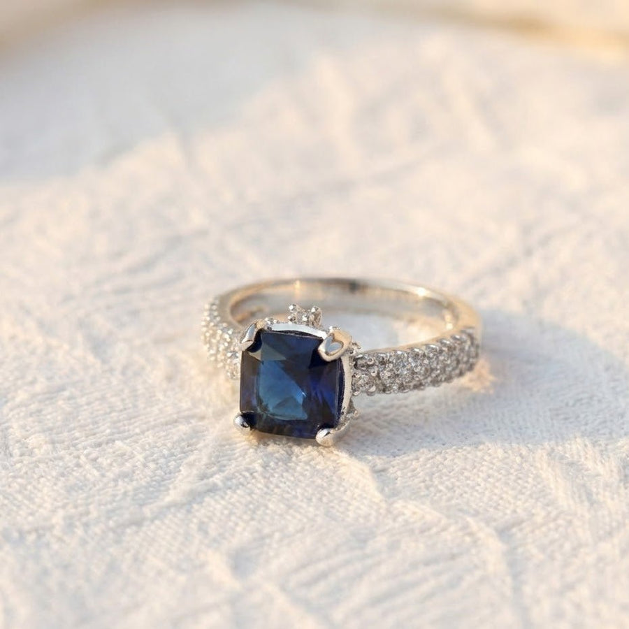 Silver cocktail ring with royal blue cushion-cut gemstone placed on white textured fabric