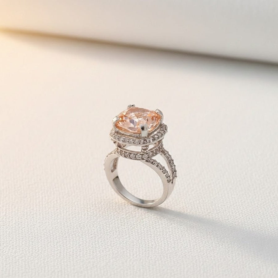 Peach cushion-cut gemstone ring with double pavé halo and split silver-tone band on light background
