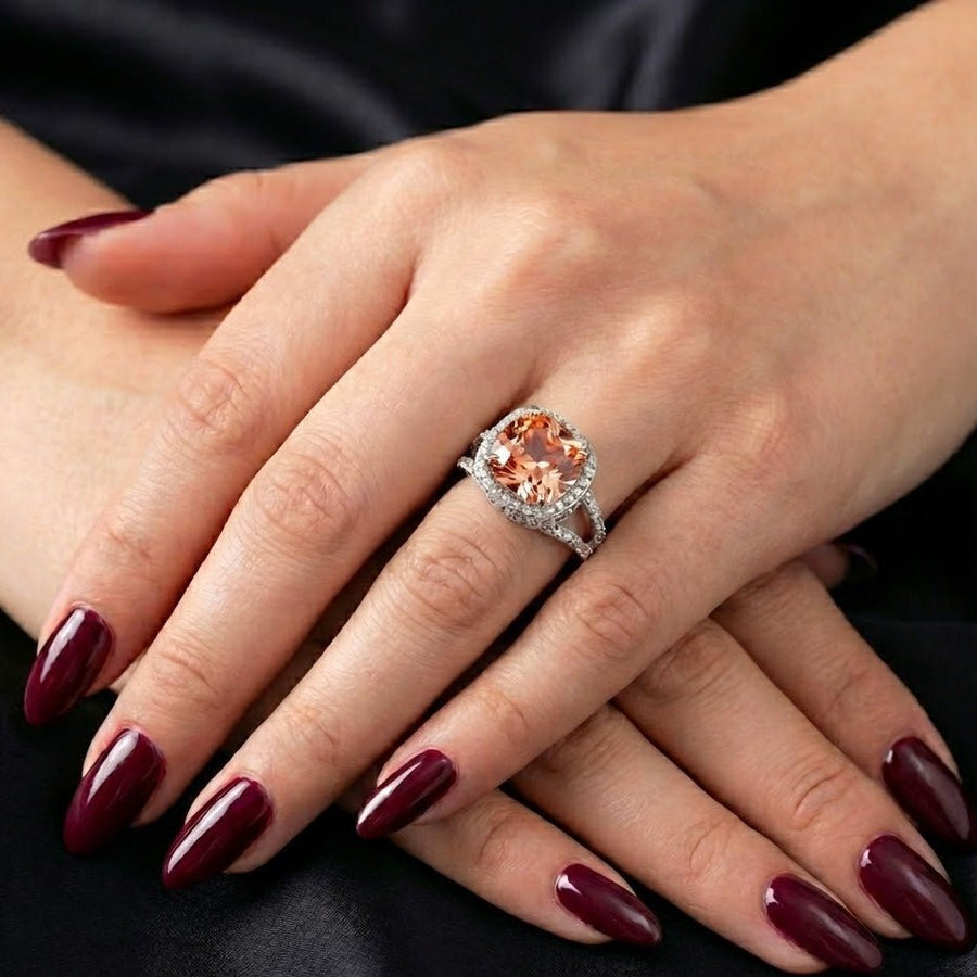 Women's hand modeling cushion-cut peach gemstone pavé ring with dark red manicure