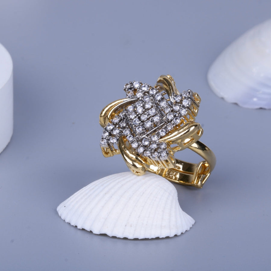Detailed view of a gold ring embellished with clear crystals resting on a white seashell against a light gray background