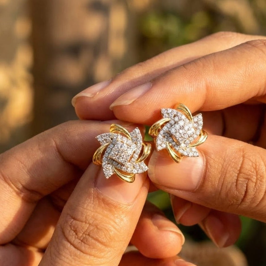 Hands holding a pair of gold and crystal floral stud earrings against a blurred natural background