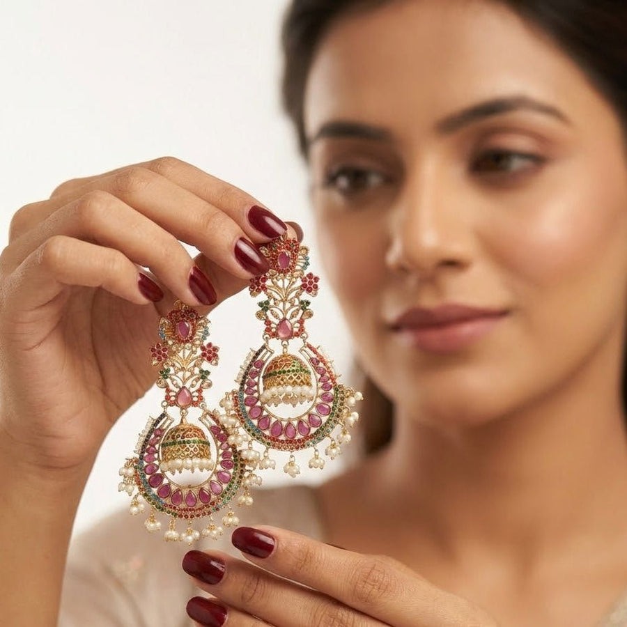 Woman holding traditional jhumka earrings showcasing intricate stonework and pearl details, highlighting craftsmanship and design