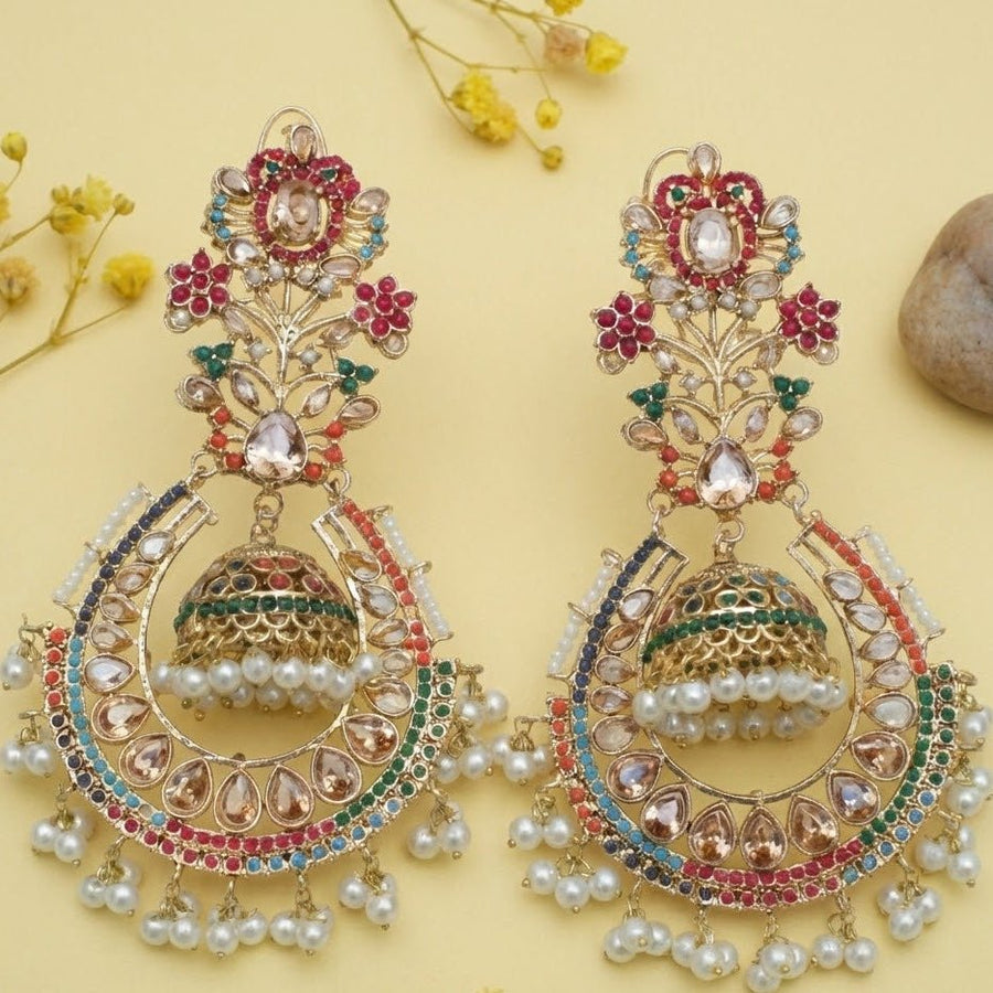 Close-up of traditional jhumka earrings with clear and pink stones held by a woman to showcase details and color