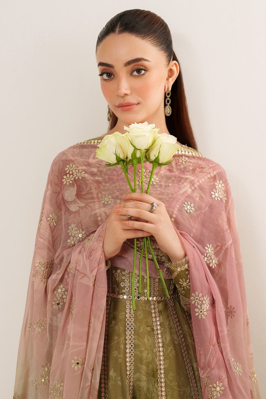 Close-up of woman holding white roses wrapped in soft pink embroidered dupatta with gold floral details