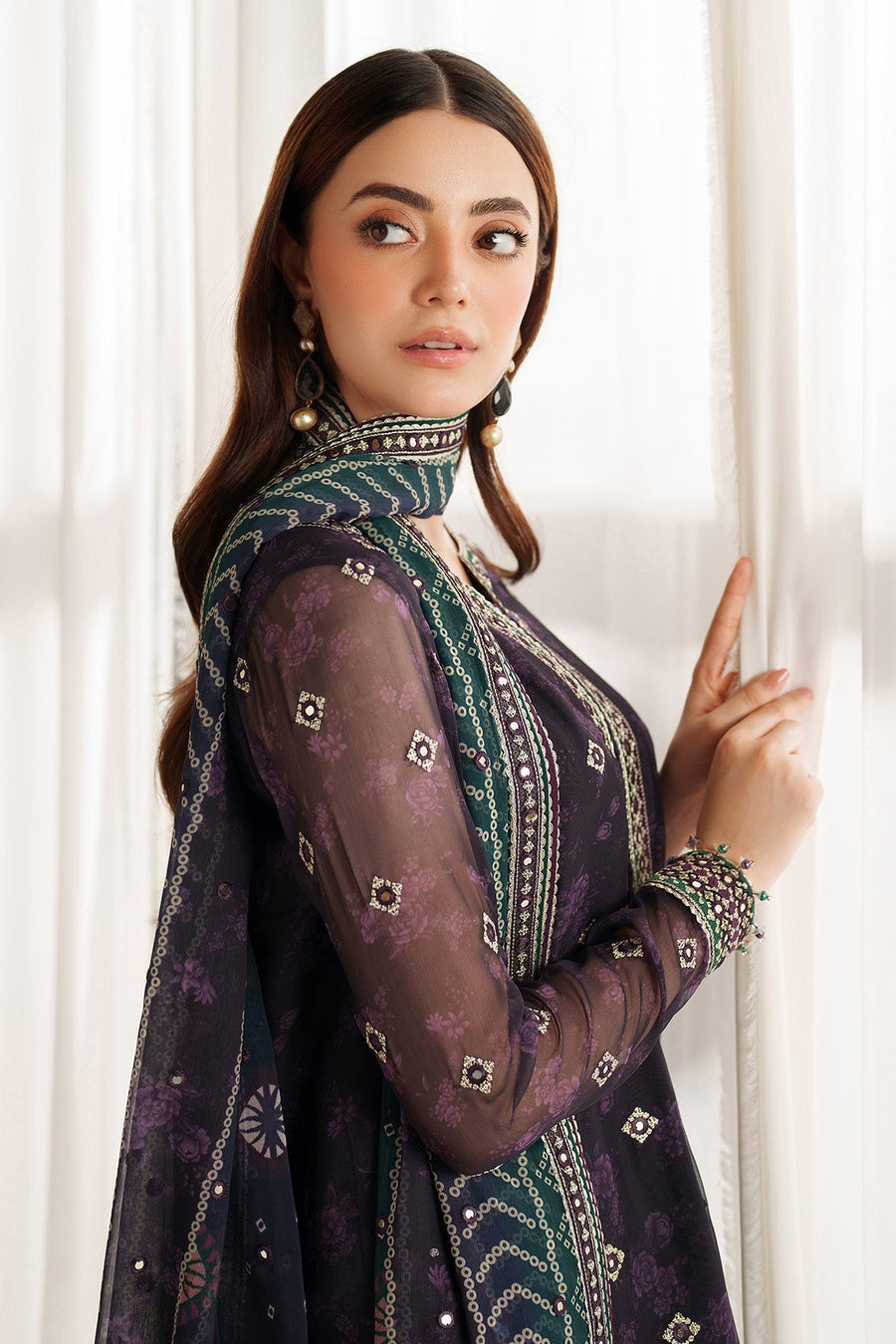 Model sitting and holding a white rose while wearing an embroidered purple suit with detailed cuffs