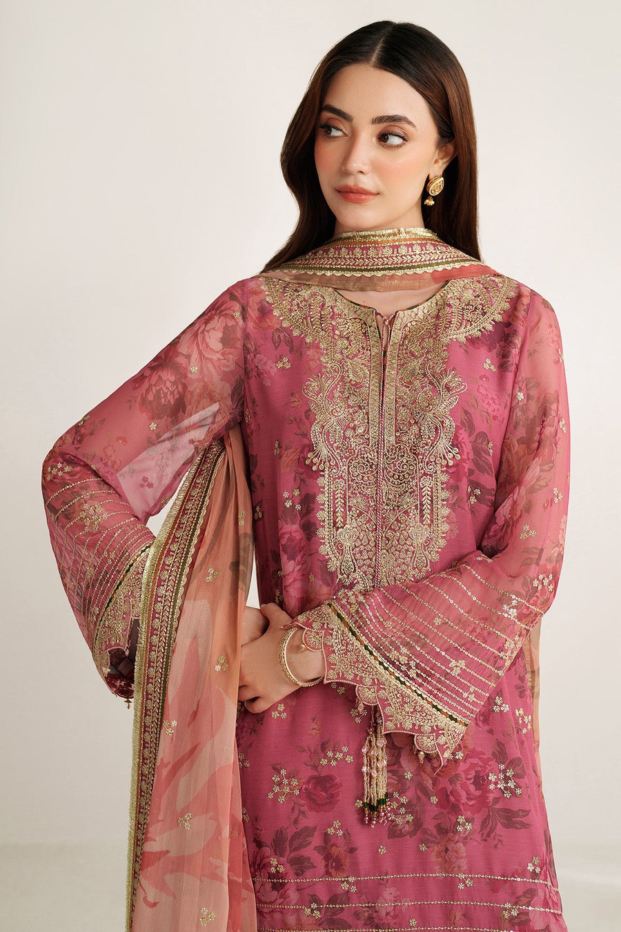 Half-length portrait of woman in mauve-pink suit looking down with subtle makeup and gold earrings