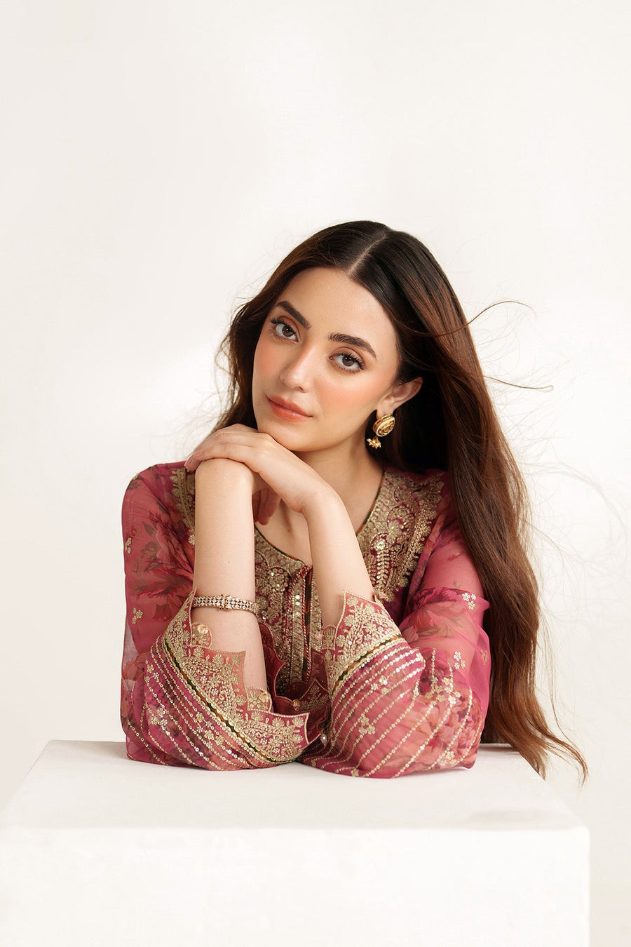 Woman resting on white surface wearing mauve-pink suit showcasing detailed embroidery on neckline and sleeves