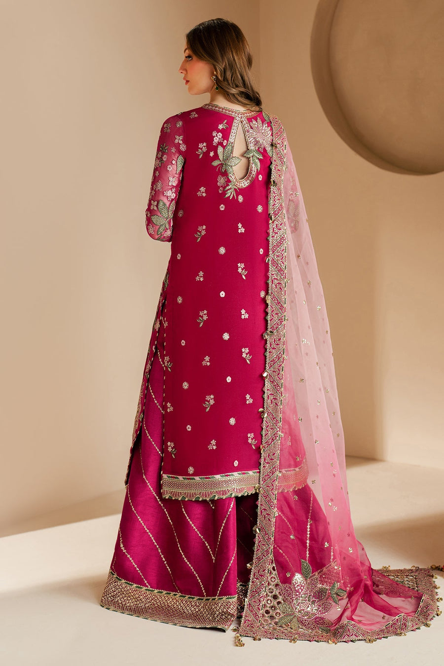 Closeup of model displaying intricate embroidery on front of magenta formal suit with pink sheer dupatta draped