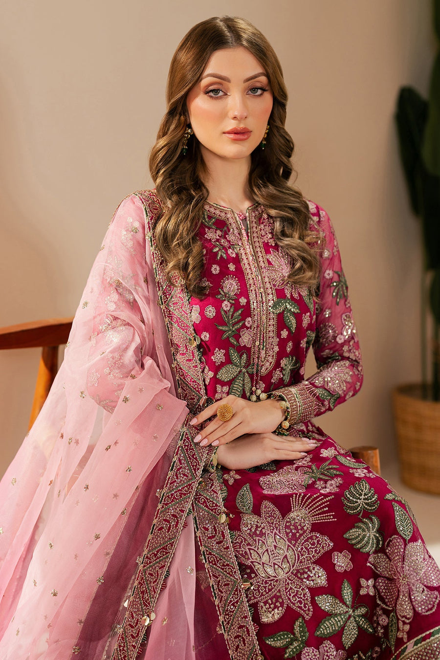Model posing in embroidered magenta formal suit with flowy sheer pink dupatta and traditional rings