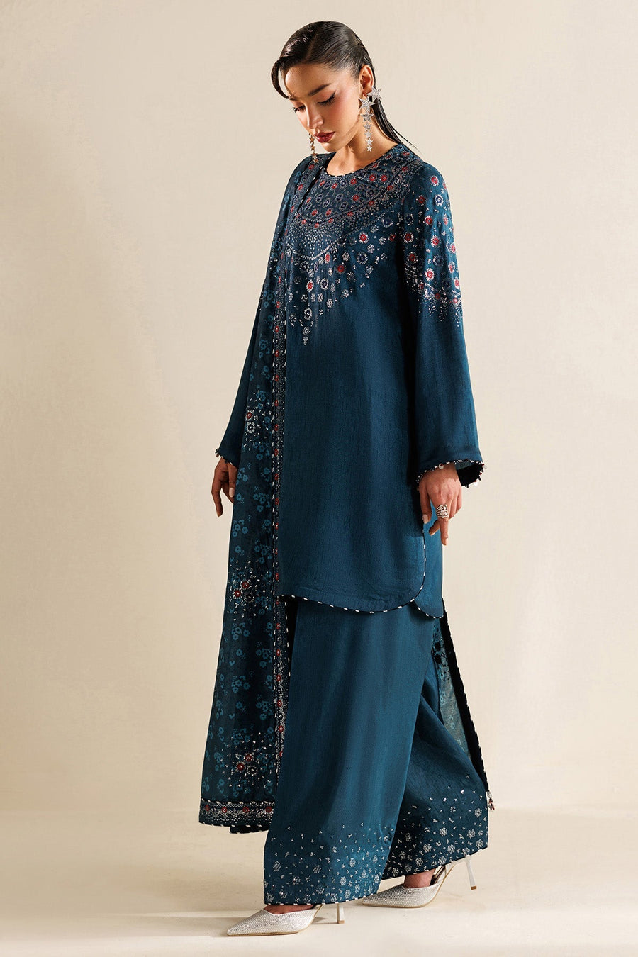 Side view of woman in teal embroidered unstitched suit showing embroidery details on dupatta and trouser hem.