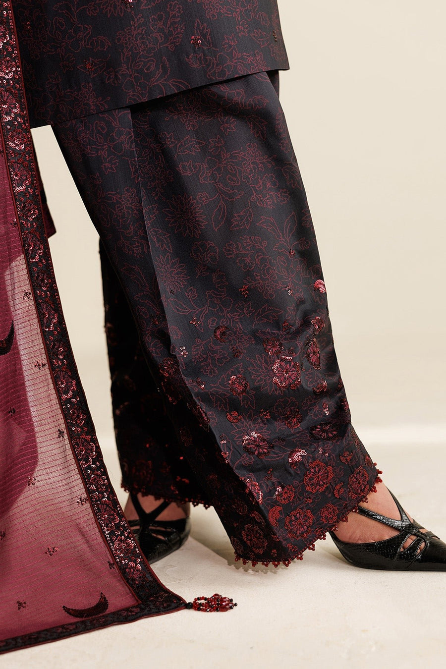 Model’s hand showing beadwork on sleeve cuff with maroon embroidered floral designs and sequin details on black fabric.