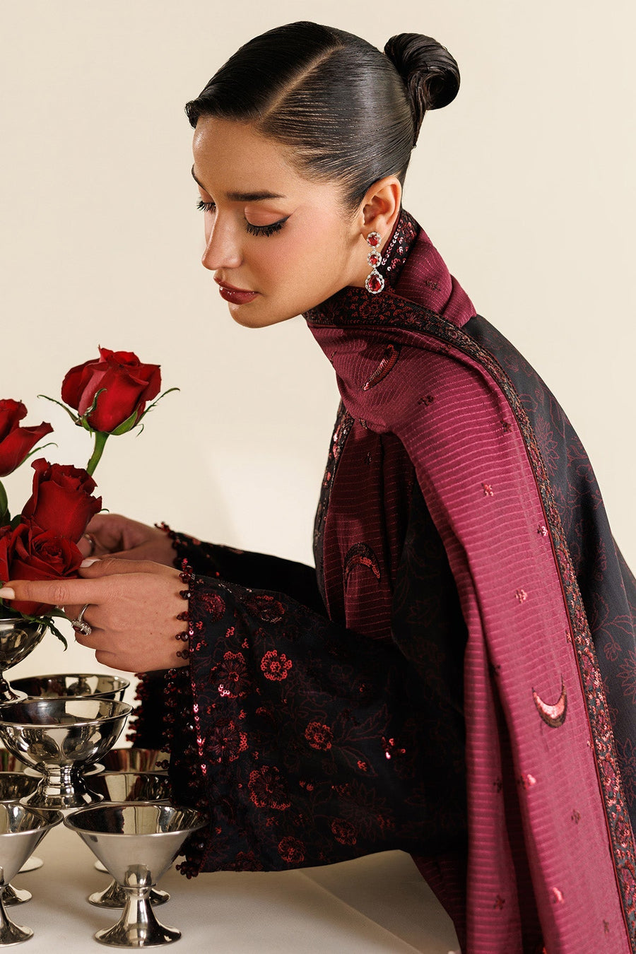 Model holding bouquet of red roses while showcasing embroidered black kameez and maroon dupatta with crescent sequin embroidery.