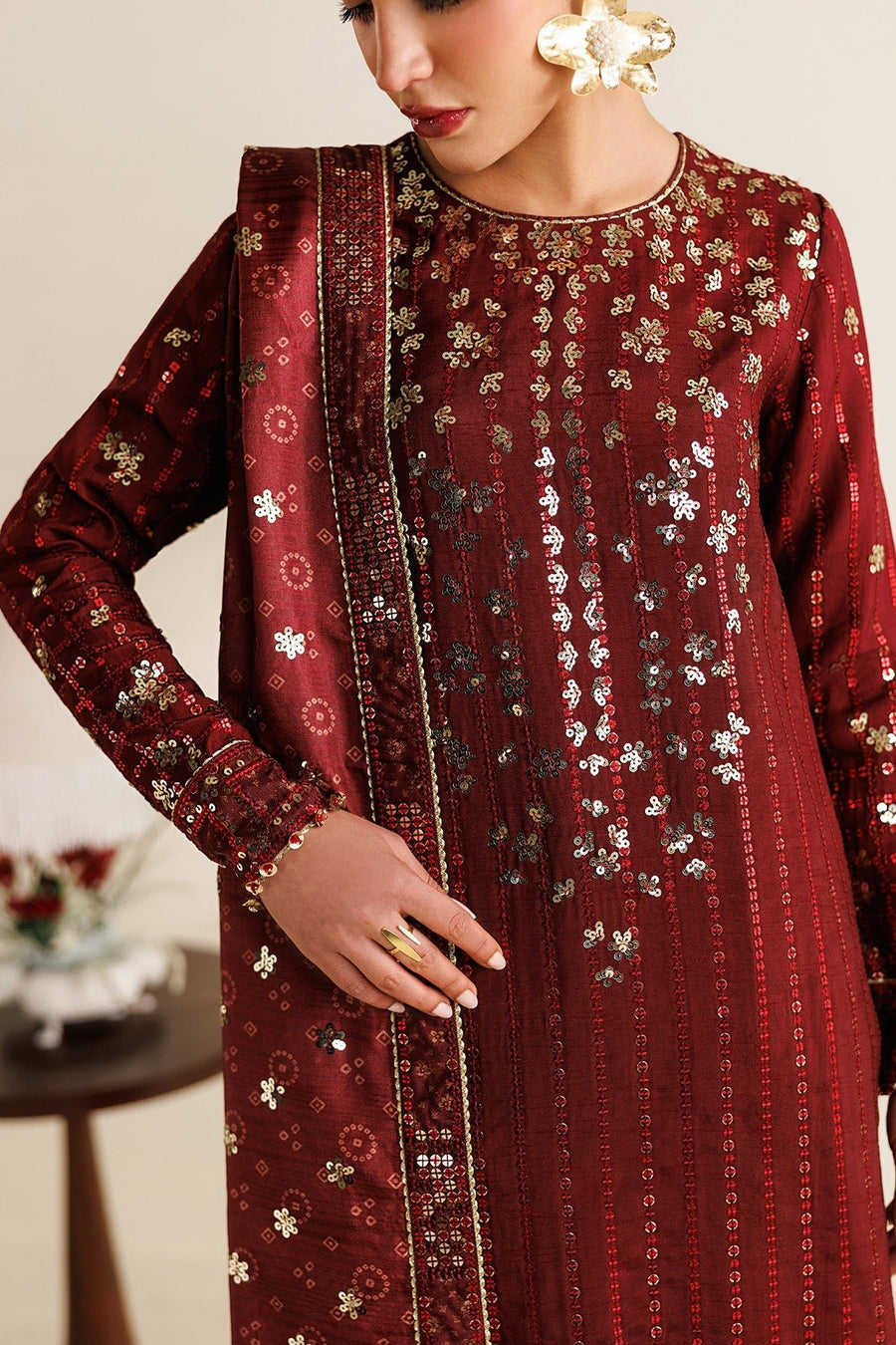 Side profile of woman in embroidered maroon suit and dupatta, displaying sequin and beadwork on cuffs and hem