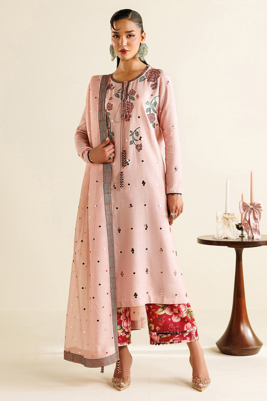 Woman standing in pink embroidered traditional suit with floral embroidery, sequin embellishments, and red floral pants, draped in light pink dupatta