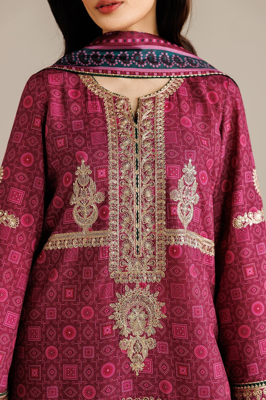 Rear view of model holding down a sheer printed dupatta showing full back design and embroidered trouser hems on the deep magenta suit.