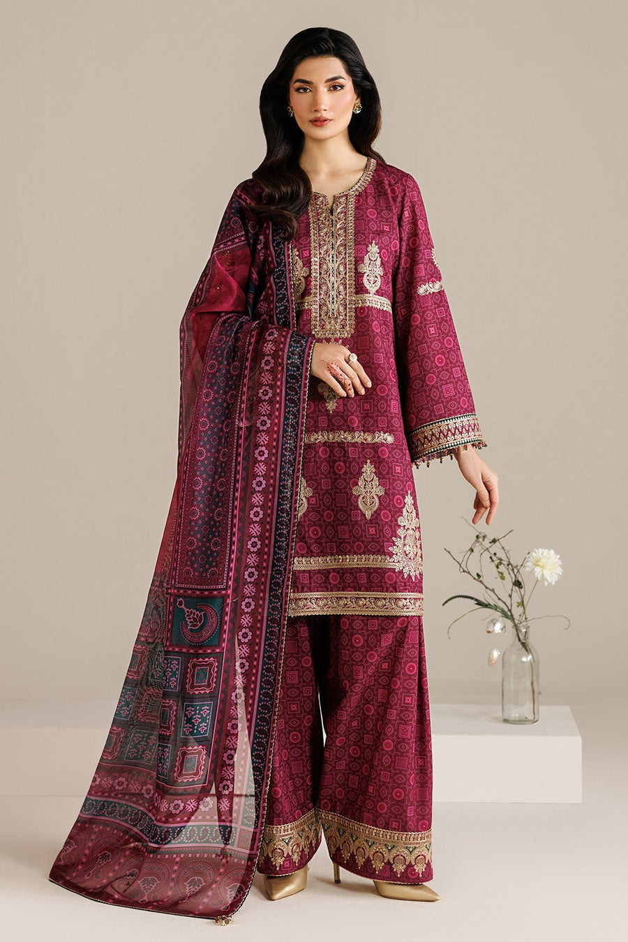 Full front view of model standing wearing unstitched deep magenta embroidered suit with coordinating dupatta and wide-legged trousers, styled with gold heels.