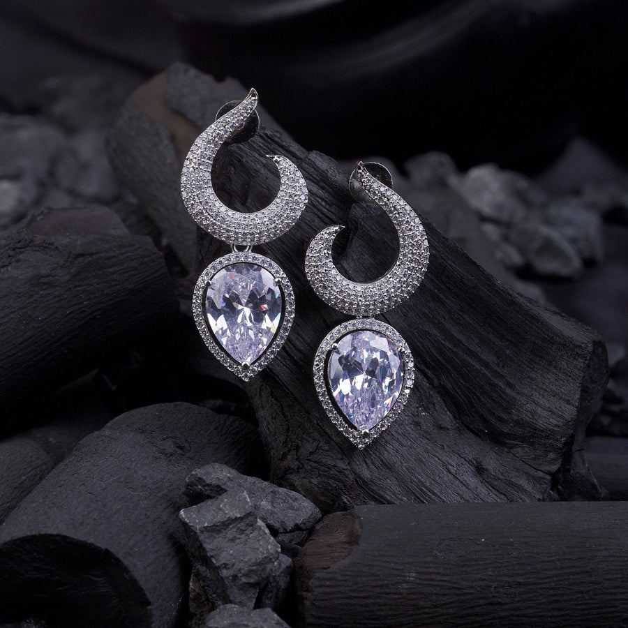 Silver-plated earrings with clear teardrop stones resting on black charcoal pieces