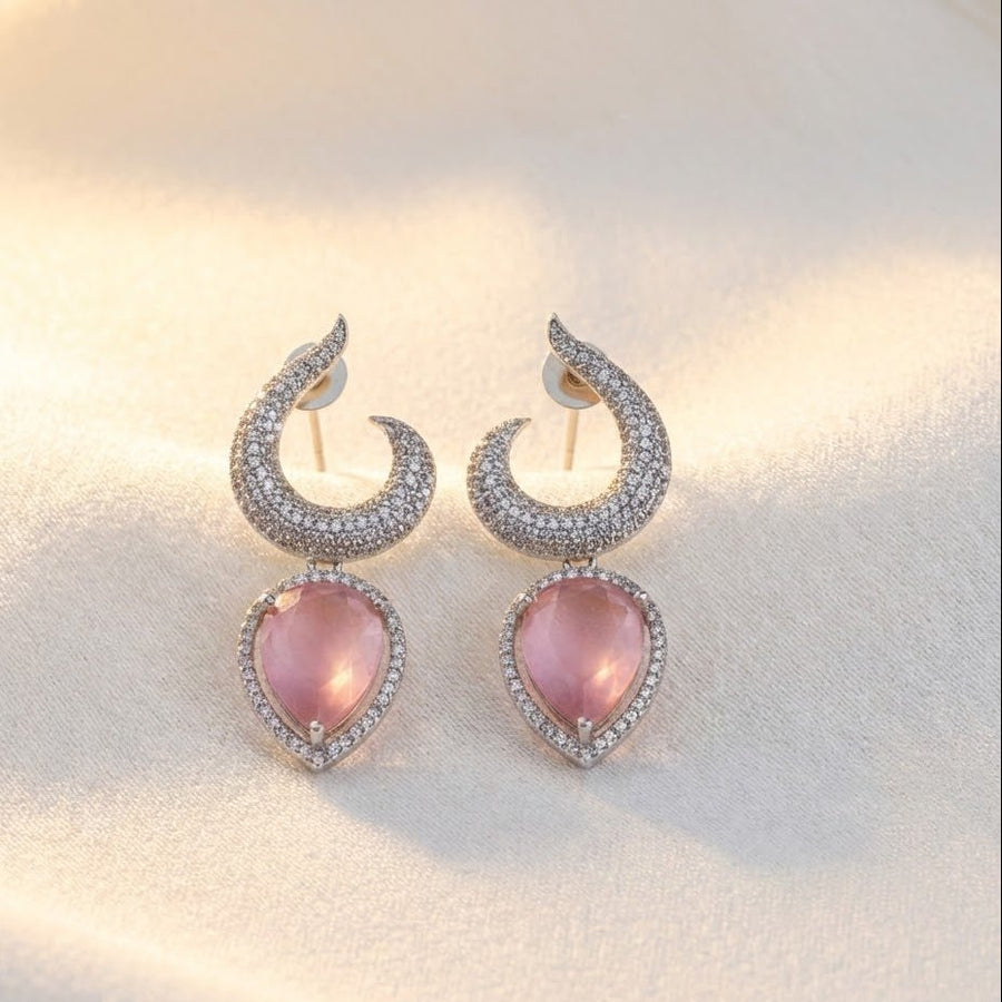 Hand holding silver-plated earrings with pink teardrop gemstones in sunlight