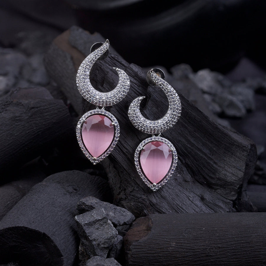 Silver-plated earrings with pink teardrop gemstones placed on black charcoal pieces