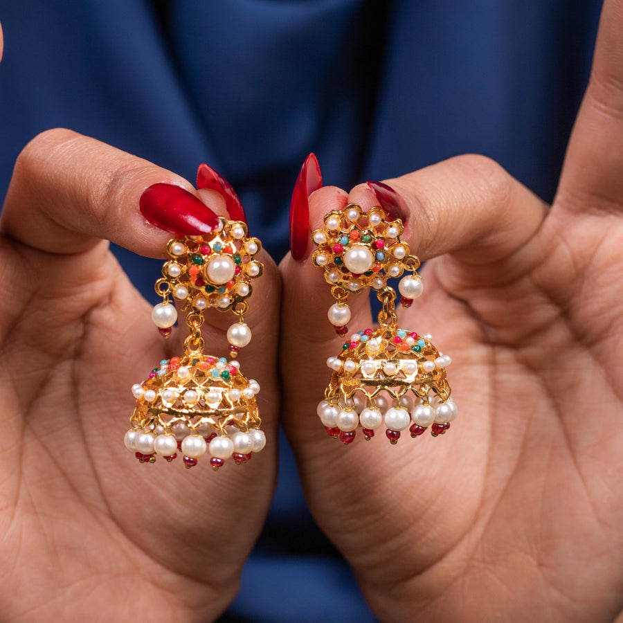 Close-up of hands holding traditional Pearl Chandbali earrings with gold-tone metal, multi-colored stones, and dangling pearls
