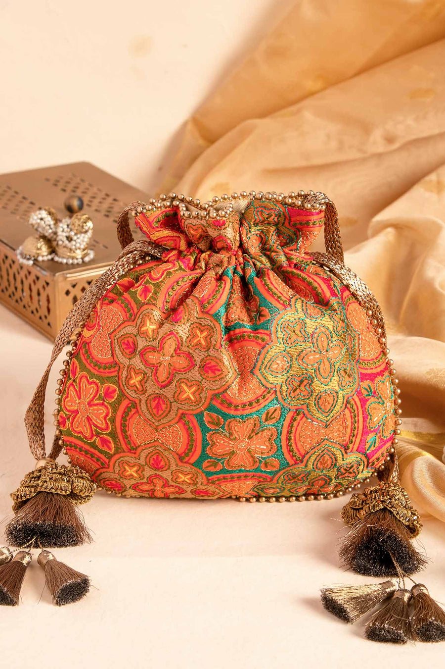 Vibrantly embroidered orange potli bag with gold tassels and intricate floral patterns on silk fabric