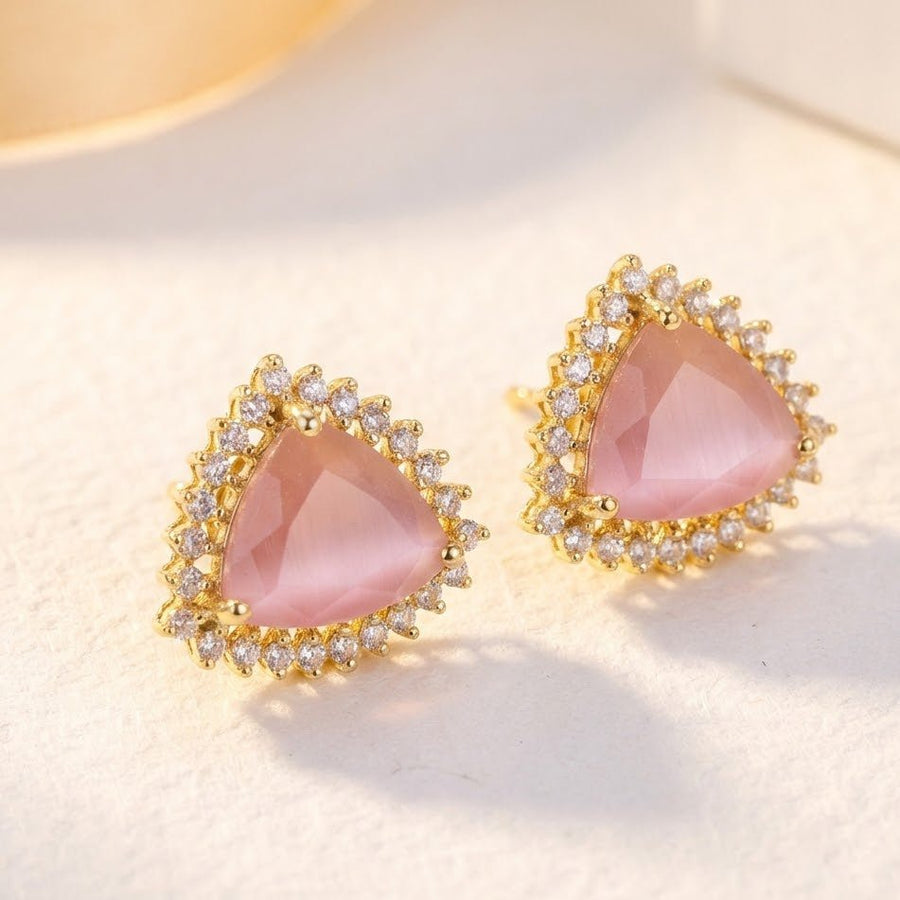 Soft pink trillion cut gemstone halo stud earrings on white surface under warm natural light