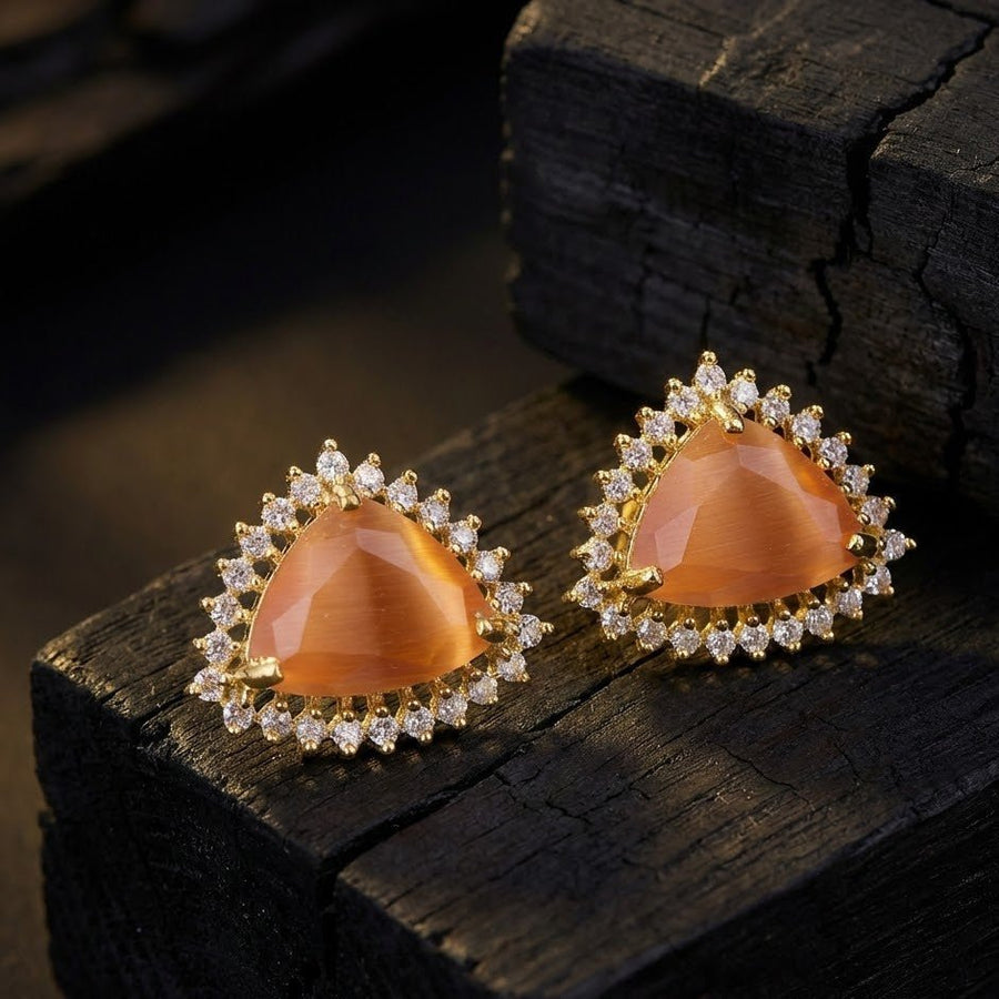 Amber-toned trillion cut gemstone halo studs displayed on black textured background