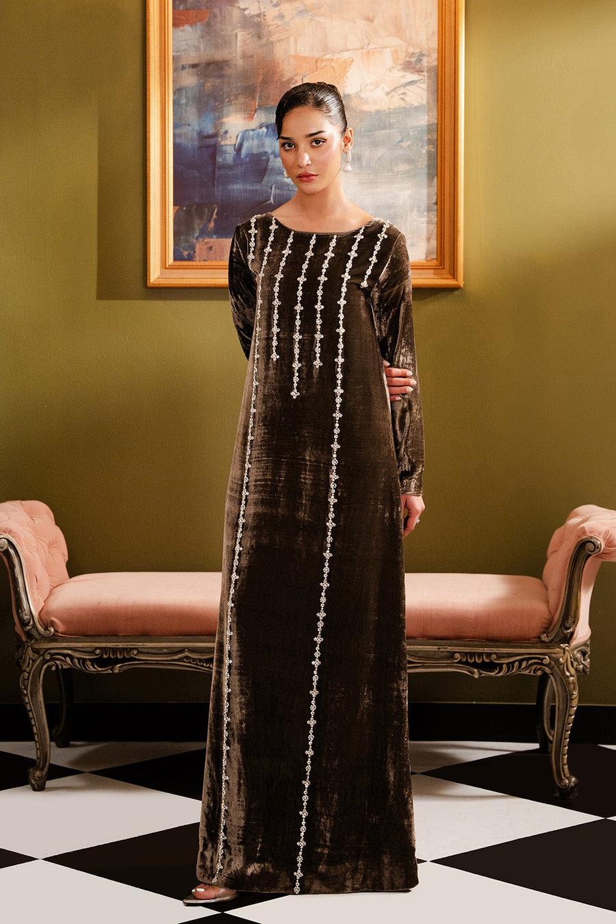 Woman wearing a full-length mud grey velvet dress with vertical pearl and crystal embellishments standing in an elegant room with green walls and classic furniture