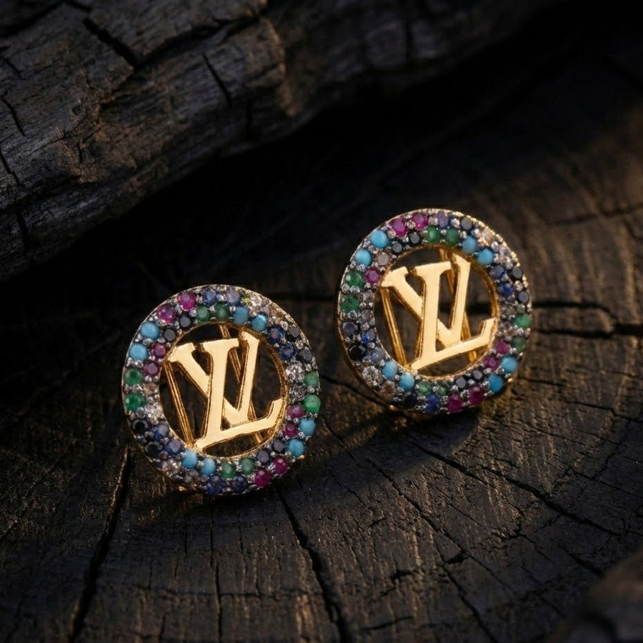 Close-up of gold-tone round earrings with multicolor stones and prominent logo centerpiece on rustic wooden surface