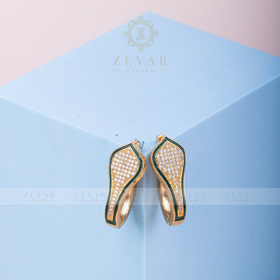 Pair of gold tone teardrop-shaped hoop earrings with green enamel border and pavé stone detailing displayed on light blue geometric stand