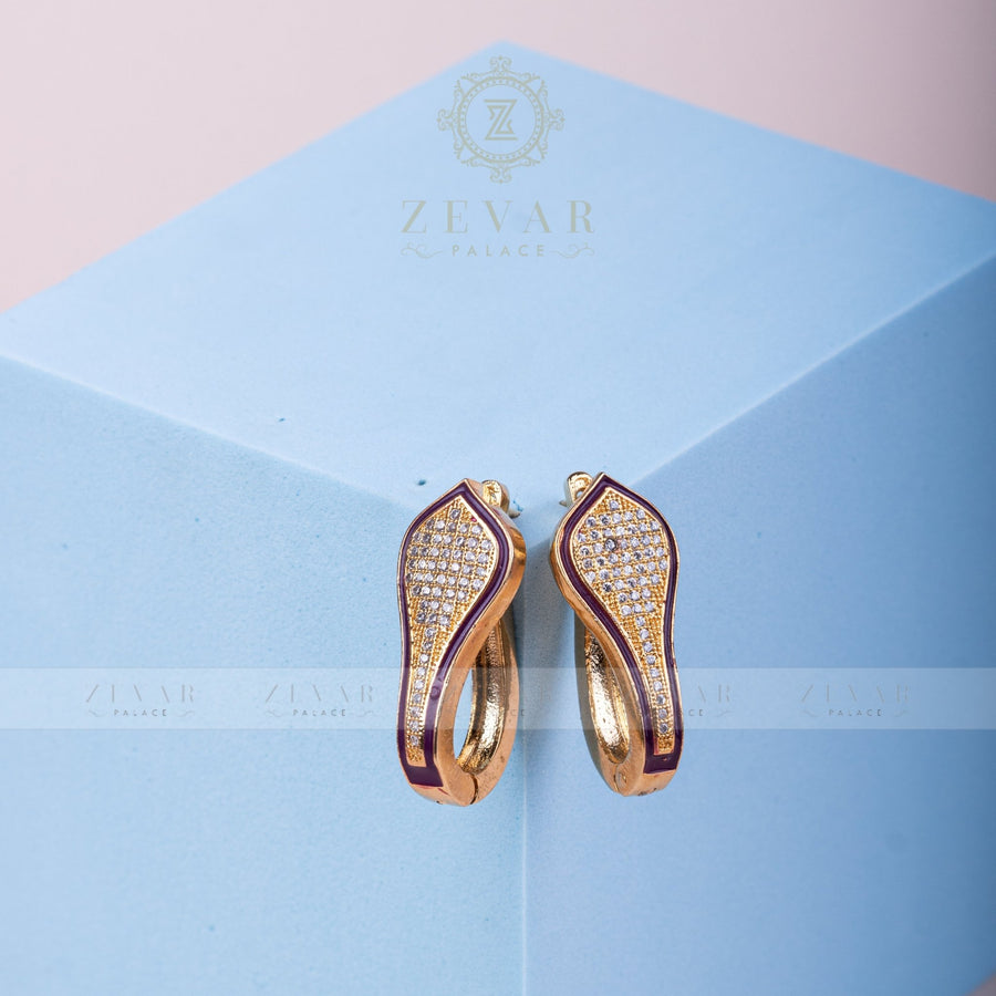 Pair of gold tone teardrop-shaped hoop earrings with green enamel border and pavé stone detailing displayed on light blue geometric stand, alternate angle