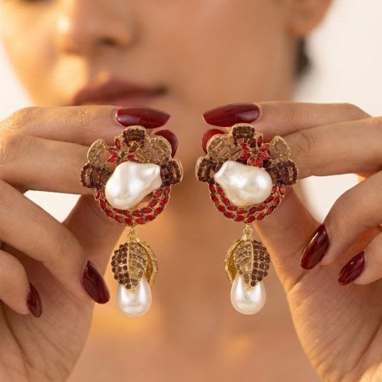 Hands holding ruby red drop earrings with white baroque pearls