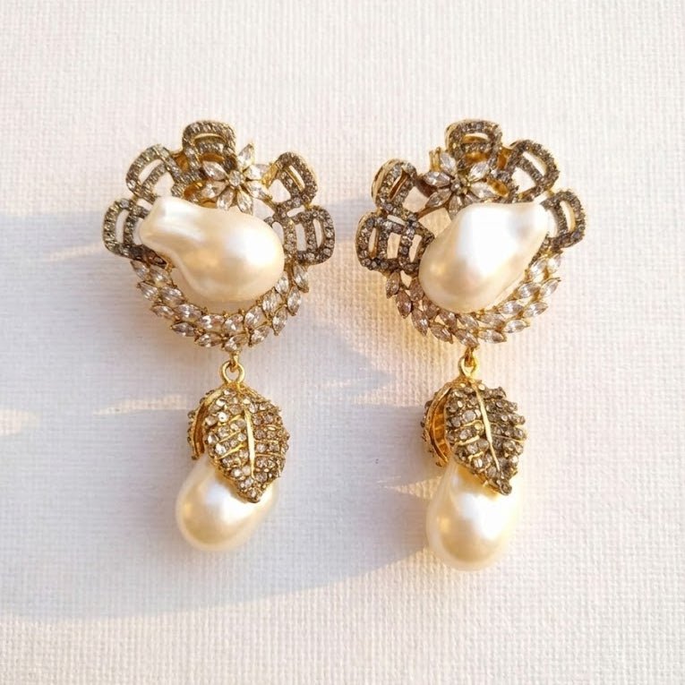 Close-up of gold drop earrings with white pearls and crystal leaf design laid on fabric