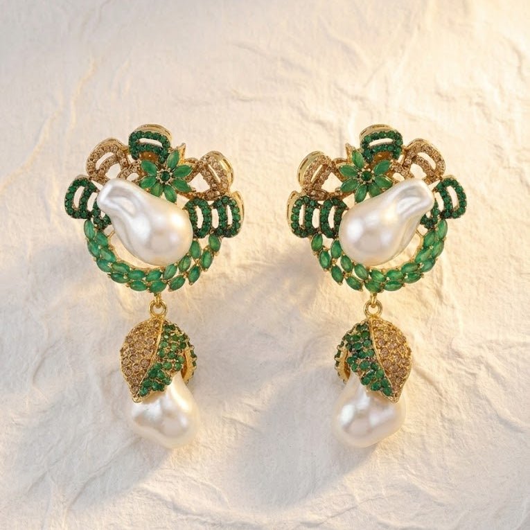 Emerald green stone accented gold drop earrings photographed on textured fabric