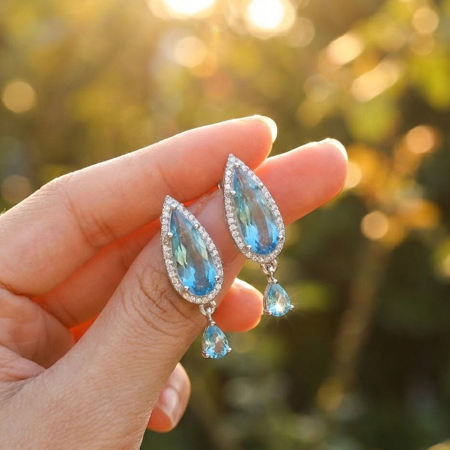 Woman with blonde hair wearing blue crystal drop earrings outdoors with sunlight highlighting the jewelry
