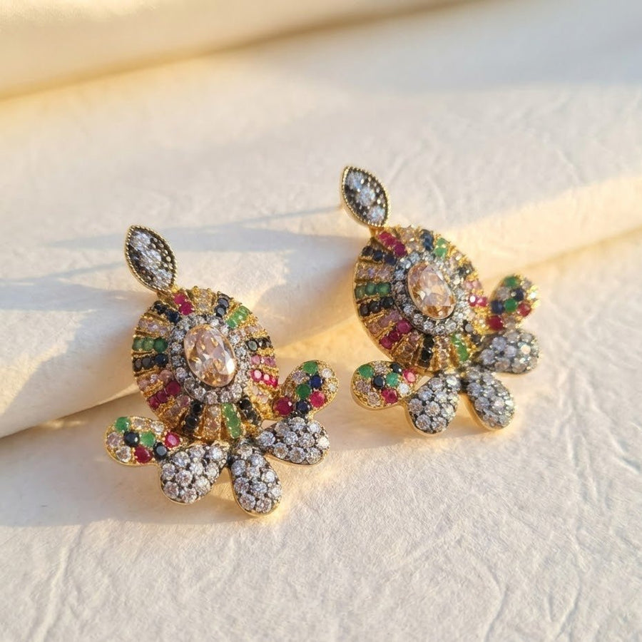 Sapphire blue floral gemstone stud earrings displayed on beige fabric with pebble stones