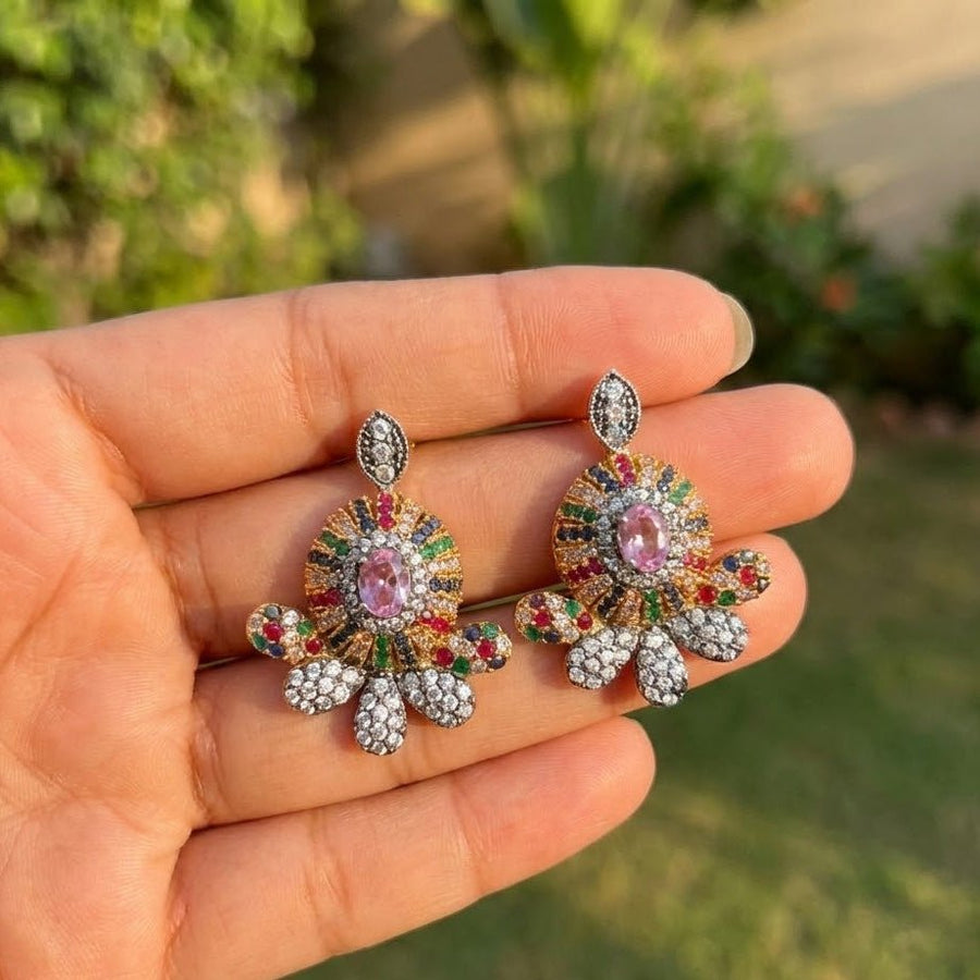 Hand holding emerald green floral gemstone stud earrings with outdoor garden background