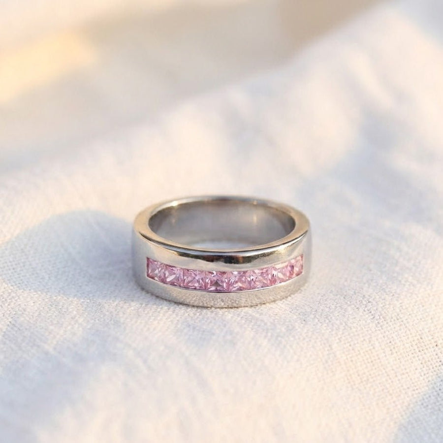 Silver band ring with pink stones placed on soft white fabric, emphasizing polished finish
