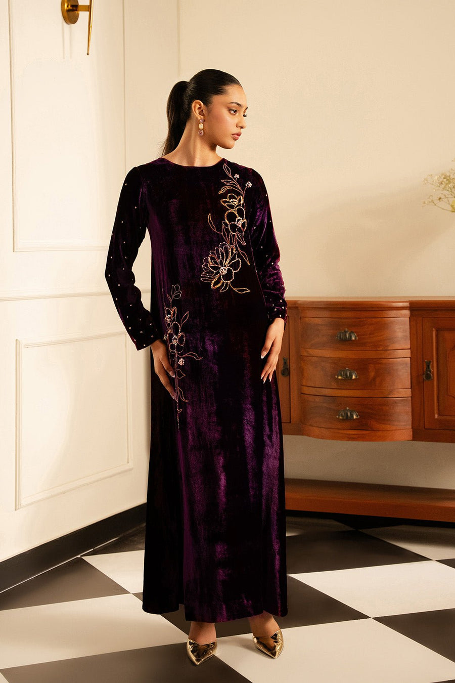 Model wearing a deep purple velvet formal dress with floral jewelled embroidery standing in a stylish interior.