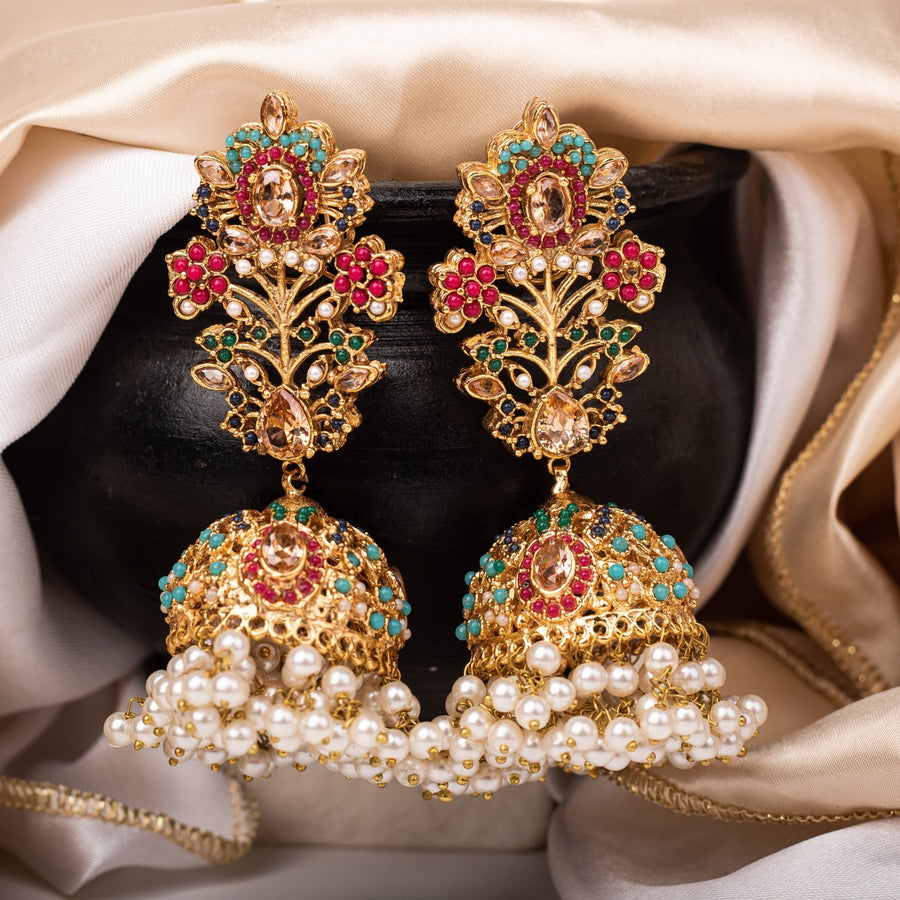 Pair of Royal Garden Jhumka earrings featuring peach-colored gemstones with colorful accents and pearl clusters hanging from the jhumka dome on a beige fabric background