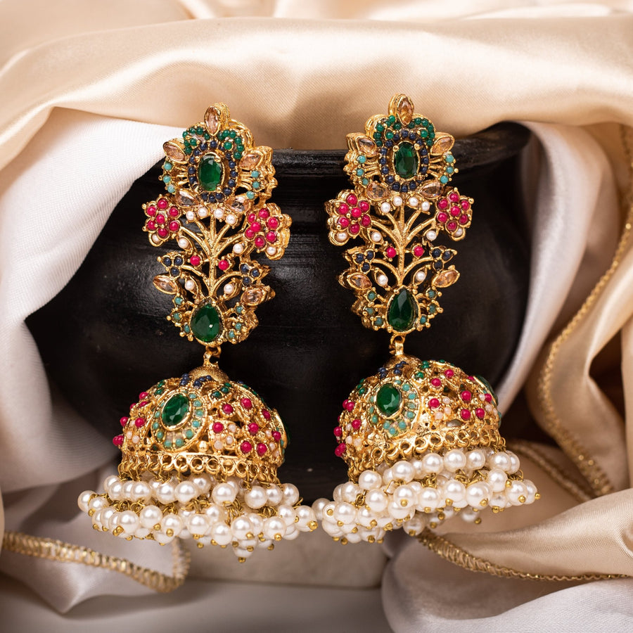 Pair of Royal Garden Jhumka earrings with green, red, blue, and turquoise gemstones and pearl clusters displayed on a black pot with beige fabric background