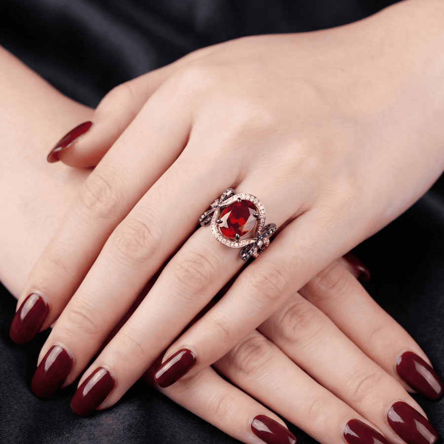 Close-up of rose gold ring with a large oval pink gemstone, clear halo stones, and black oxidized bow design on band sides