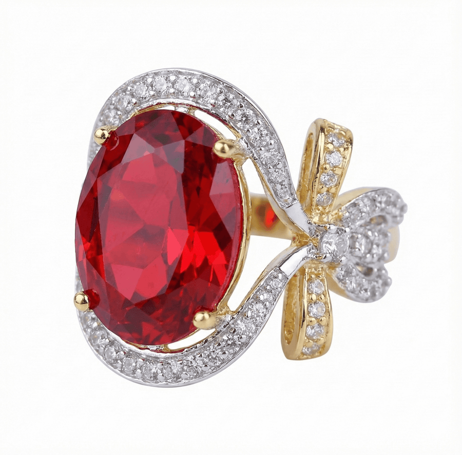Close-up of a gold and silver ring with a large red oval semi-precious gemstone surrounded by sparkling cubic zirconia and a bow detail