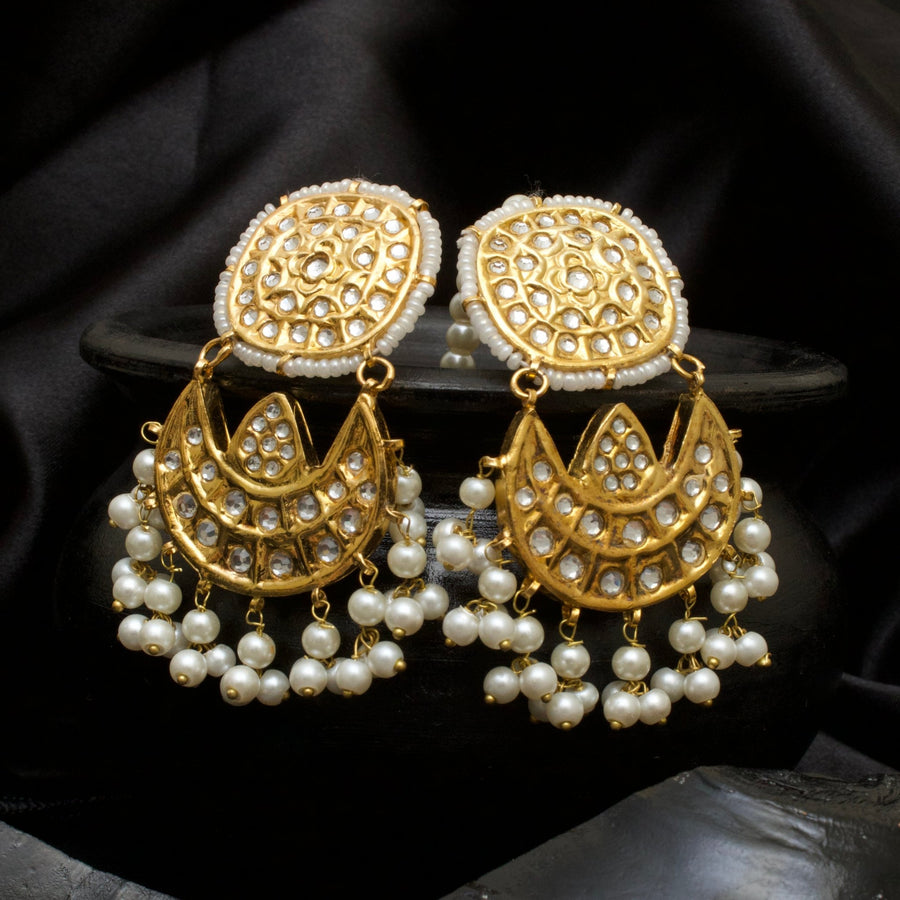 Close-up of gold-toned Kundan Jhumka earrings with kundan stones and white pearl tassels displayed on a black pot with black satin background