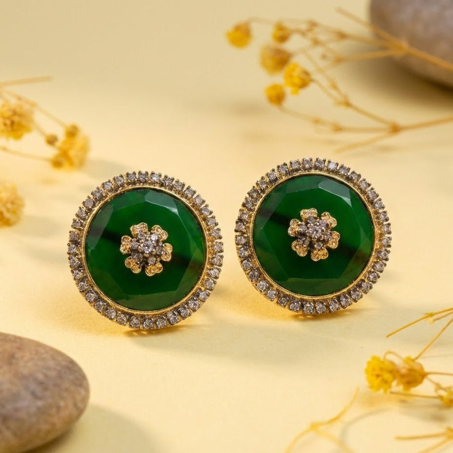 Emerald green faceted stone round stud earrings with flower motif surrounded by sparkling stones against white background
