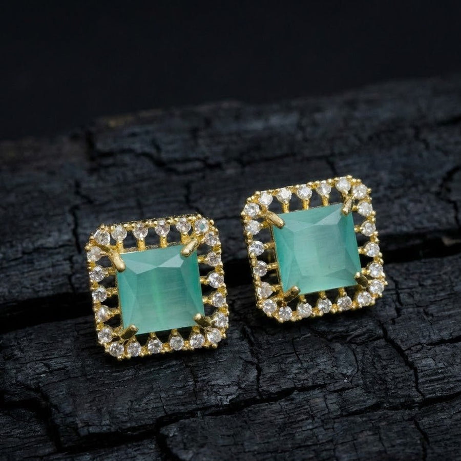Mint green square halo stud earrings placed on textured dark surface to emphasize sparkle and metal details