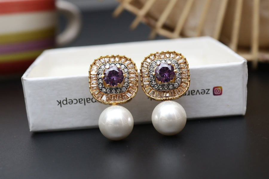 Pair of gold-tone earrings with purple central stones accented by crystals and large pearl drops